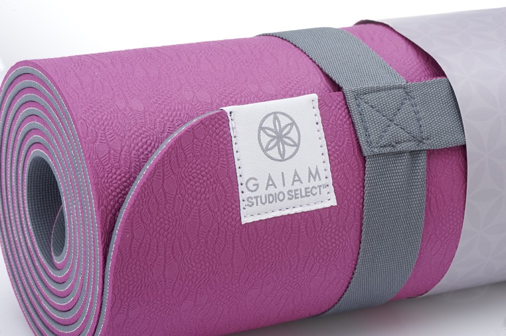 Close-up of a rolled pink Gaiam Studio Select mat with a woven label and grey strap