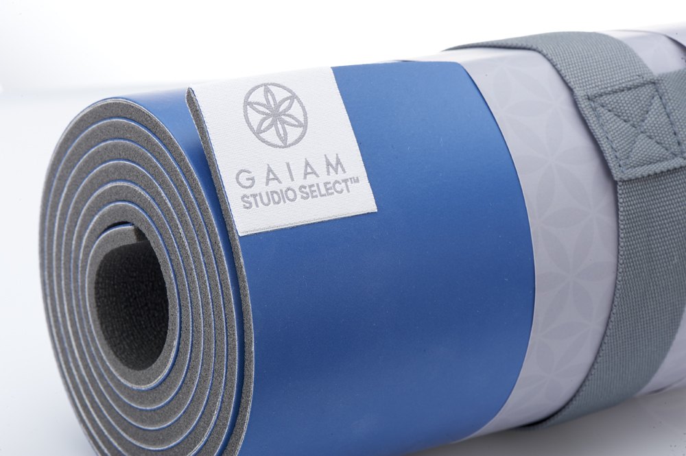 Close-up of a rolled blue Gaiam Studio Select mat with a white label and grey strap