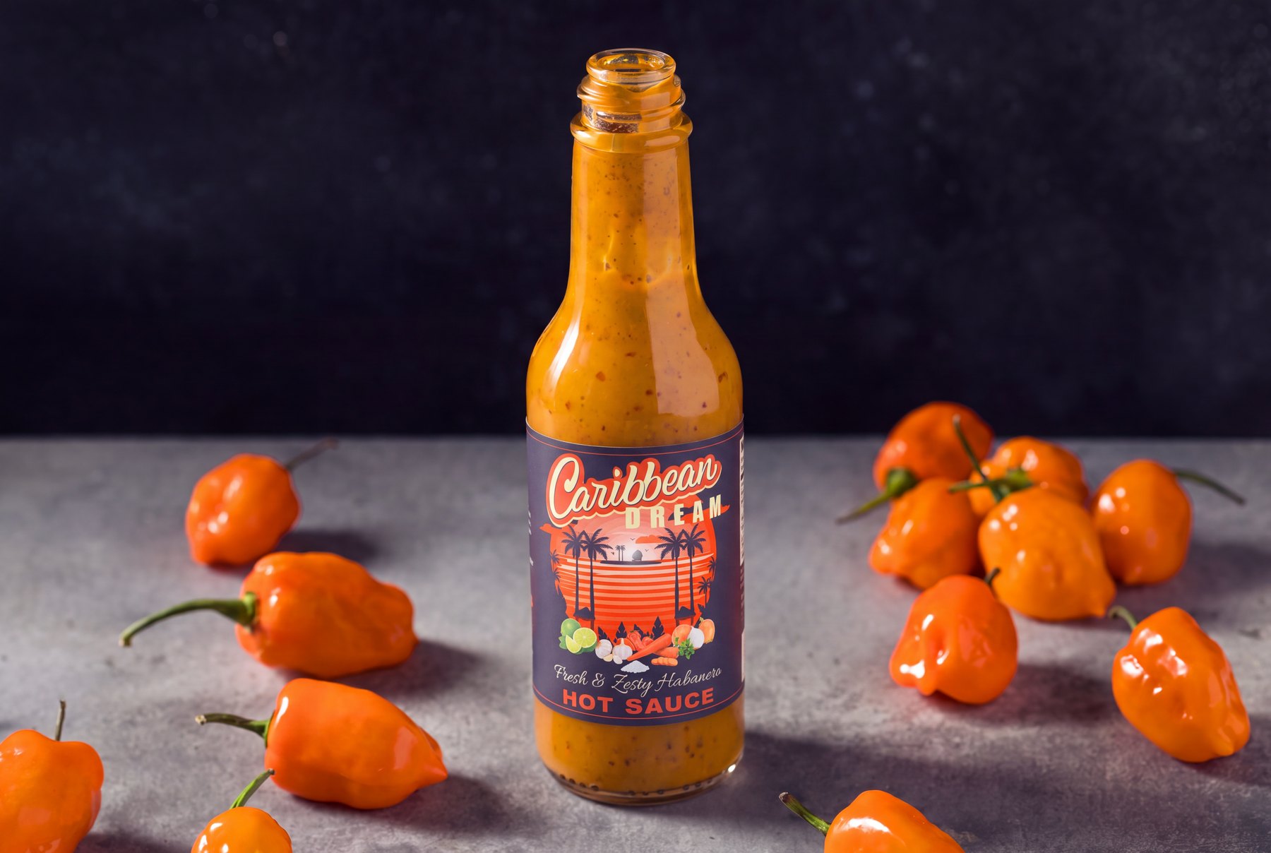 Open bottle of Caribbean Dream habanero hot sauce with the label applied, surrounded by orange habanero peppers
